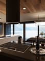 Modern kitchen with wooden ceiling, large windows with a scenic view, induction cooktop, kitchen island with bar stools, and decorative lighting fixtures.
