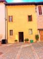 yellow brick building, wooden door, three windows, brick paved courtyard, plants