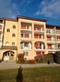 yellow apartment building with many balconies, red shutters, red roof, multiple floors, shrubs in front