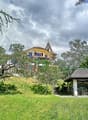 House on a hill, surrounded by trees, spacious lawn, small wooden house, steep stairs, white exterior, red trims