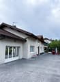 Detached house, white exterior, tiled roof, double glass doors, small table with chairs, outdoor seating area, paved driveway