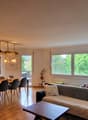 Living room with dining area, wooden floor, fireplace, sofa, coffee table, chandelier, dining table with chairs, window with view
