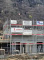 Construction site of a house in progress, surrounded by scaffolding, featuring large windows and door frames, a crane is present to lift materials