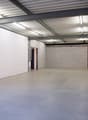 Large open space with white brick walls, a concrete floor, and a metal ceiling with exposed beams and lighting fixtures. The space appears to be a warehouse or industrial facility.