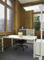 A room with a desk, swivel chair, floor lamp, large windows, wooden walls, office storage, and a radiator.