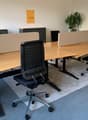 Empty office space with desks, office chairs, wall-mounted frames, and a potted plant.