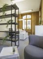 Office with wooden paneled walls, white ceilings, open layout, floor-to-ceiling windows, shelves, black chair, white desk, potted plants