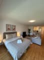 a bedroom with a large bed, two nightstands, a couch, a television, a microwave, a desk, and a dining table with chairs