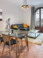 Living room with wooden floor, glass table, dining chairs, glass windows, sofa, pillows, painting, rug, and a lamp