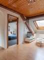 modern apartment with wooden floors, wooden beam ceiling, cozy living room with couch, TV, desk, bedroom with bed, microwave on stand, bedroom with skylight