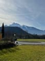 green grass, gravel path, wooden house, mountains in the background
