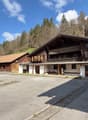 A large wooden chalet-style building with a parking area in front, surrounded by a forested mountain landscape.