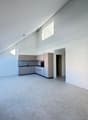 Empty room with white walls, gray floor, kitchen area with cabinets, sink, and oven, glass door, skylights