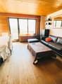 Spacious living room with wooden walls and ceiling, large windows, leather sofa, coffee table, and a balcony or terrace visible.