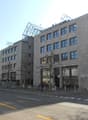 Commercial building, glass windows, grey walls, multiple floors, people walking, street lights, parked car