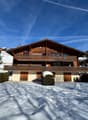 wooden exterior, wooden balconies, snow on ground, nearby trees, slope behind