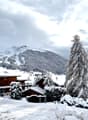 Snowy mountain landscape with several wooden chalets, trees covered in snow, and a wide snowy mountain in the background