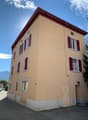 A beige building with 7 windows, red shutters, white accents and a red roof