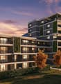 Modern multi-story residential building, balconies, green walls, surrounding greenery, bicycles parked