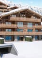 multi-level chalet with balconies, wooden exterior, set on a snowy hillside with a mountain backdrop