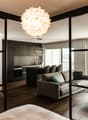 modern living room with glass walls, wooden floor, gray couch, coffee table, kitchen with island, dining table, balcony