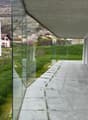 Modern building with glass walls, concrete ceiling, concrete pathway, green grass, mountain view