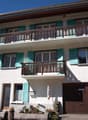 2-storey house with turquoise shutters, wooden garage door, 2 balconies, greenery around