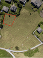 Aerial view of a plot of land with surrounding houses and green areas.