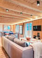 Open-plan living area with wooden beams, large sofa, center table, wooden floors, balcony, large windows