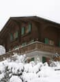 2-story wooden chalet-style house with a balcony, covered in snow in a winter landscape