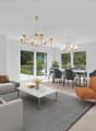 Open living and dining room, large windows, balcony, chandelier, large gray sofa, white marble coffee table, orange chair, round dining table with chairs