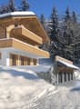 Detached house, wooden and white structure, with wooden balcony on upper floor, in snowy landscape