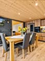wooden floor, wooden wall, TV, wooden dining table, black chairs, wooden cabinets, refrigerator, oven, countertop with flowers, toaster, wine rack