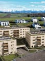 Aerial view of modern apartment buildings with green roofs and solar panels, located in a rural setting with surrounding green fields and mountain views.