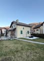 Detached house, two stories, stone facade, green windows, driveway, surrounded by grass and bushes, mountain view