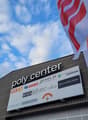Commercial building with a large sign reading 'poly center', multiple logos on the sign, and flags on poles