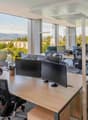 Large windows, desks, monitors, office chairs, trees and mountains view outside