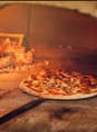 A traditional brick pizza oven with a fire burning inside, and two freshly baked pizzas on the oven floor