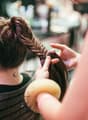 Woman with brown hair getting her hair braided by another woman