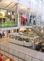 Large indoor shopping mall with multiple levels, glass walls, and various retail stores and shops visible.