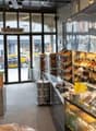 Bakery shop with glass display case, shelves, bread and pastries, tables and chairs, lamps, trash bin, and a trash chute.