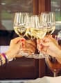 A celebration with four wine glasses raised and a bottle of wine on ice.