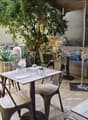 Outdoor seating area with tables, chairs, umbrellas, plants, and a chalkboard menu.