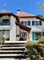 2 story house, red brick, white windows, red roof, garden, balcony, elevated ground floor, flowers, outdoor table and chairs