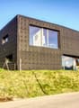 Modern house, black exterior, large windows, elevated position, surrounded by greenery