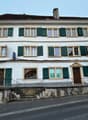 3-story house, white painted, green shutters, large windows, steps at entrance, brown door, metal railings