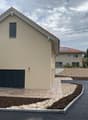 Modern 2 story house, beige, with garage, concrete driveway, gravel path, solar panels on the back house.