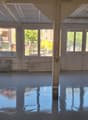 Empty room, high ceiling, multiple large windows, concrete floor, large central pillar, exterior view visible through windows