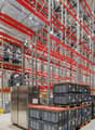 large warehouse with red and silver metal shelving, multiple stacked boxes, large silver refrigerator, concrete floor
