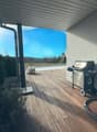 Covered outdoor patio with wooden deck, gas grill, and a view of the swimming pool and surrounding landscape.